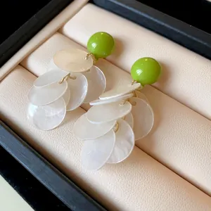Detailed view of green bead earrings with layered white shell tassel discs.