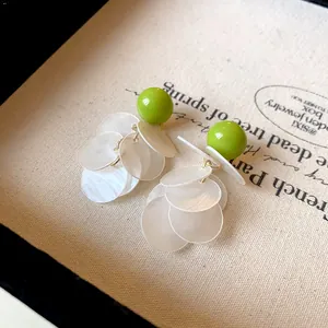 Close-up of elegant green bead earrings with layered white shell-like tassels.