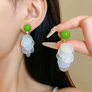 Close-up of green stud earrings with white circular shell tassels on model