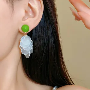 Close-up view of green button earrings with layered white shell petals on a model's ear.