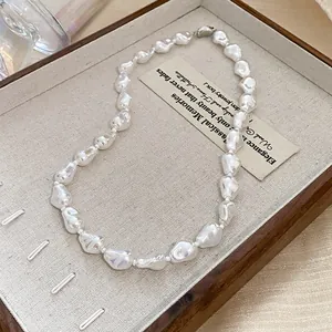 Detailed macro view of an irregular baroque pearl necklace inside a wooden jewelry tray