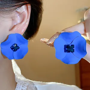 Detailed view of matte blue spray-painted flower stud earrings with a central gemstone.