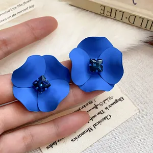 Macro view of matte blue flower stud earrings featuring dark blue square gemstone centers.