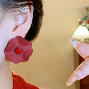 Close-up detail view of red matte flower ear stud featuring square crystal center