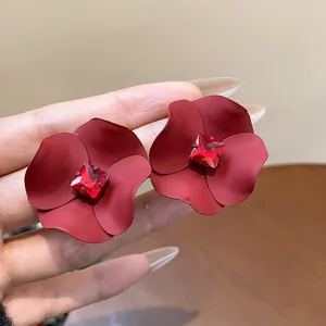 Close-up of matte red flower stud earrings with a central red square crystal detail