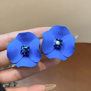 Close-up detail of blue matte flower stud earrings with central blue square rhinestone