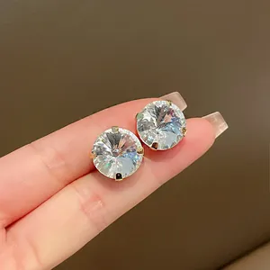 Detailed view of large round brilliant-cut crystal stud earrings held on fingertips