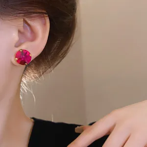 Close-up of a large round magenta crystal stud earring with gold-tone setting on ear.