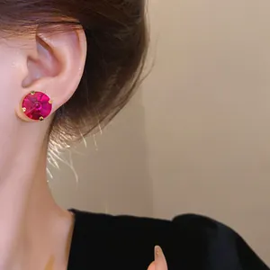 Close-up detail showing a vibrant pink crystal stud earring with gold prong setting