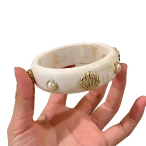 Chunky acrylic bangle with golden shell and pearl accents in marble white finish.