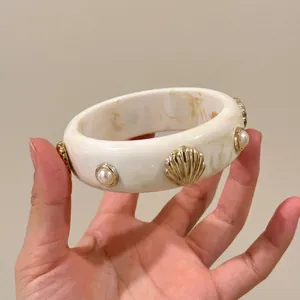 Close-up view of a chic cream marble acrylic bangle featuring gold shell and pearl accents