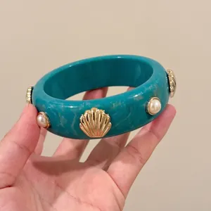 Close-up of a teal acrylic ethnic style bangle featuring gold shell and pearl charm details