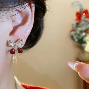 Élégantes boucles d'oreilles cerise plaquées or avec zircons sur l'oreille du modèle