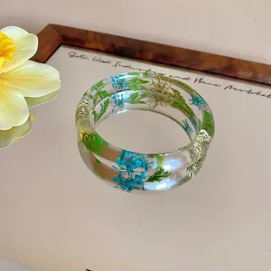 Detailed view of clear acrylic bangle with embedded blue and green dried flowers