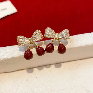 Gros plan de boucles d'oreilles cerises avec nœud en zircons et émail rouge.
