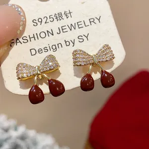Détail rapproché de boucles d'oreilles cerises avec nœud en zircon et émail rouge élégant.