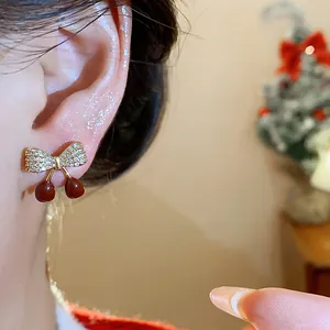 Détail de boucles d'oreilles nœud cerise avec zircons étincelants et émail rouge