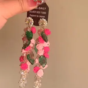 Primer plano de pendientes largos con rosas de resina rosa y borlas de cristal fino.