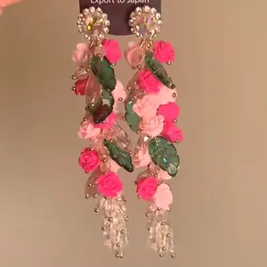 Detalle de pendientes florales con rosas rosadas y borlas de cristal brillante.