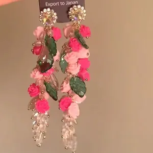 Detalle de pendientes florales de cristal con rosas rosas y hojas verdes colgantes