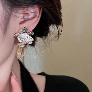 Silver textured flower stud earrings with a modern crumpled metal design worn by a model