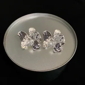 Macro shot of silver-colored wrinkled flower stud earrings with artistic metallic texture.