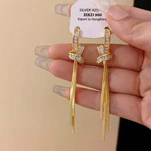 Dettaglio di eleganti orecchini placcati in oro con nodi, zirconi e lunghe nappe