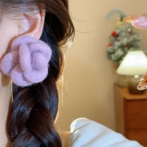 Close-up detail of a purple flocked flower earring worn by a model in warm indoor light.
