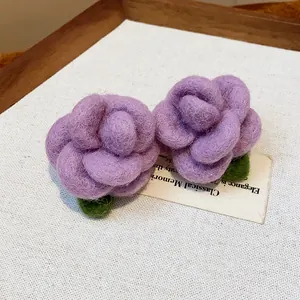 Close-up detail of handmade purple felt flower stud earrings with green leaves
