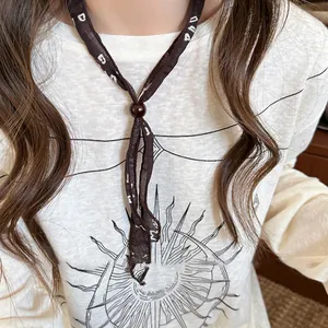 Dettaglio di collana foulard etnica in tessuto con perla marrone e motivi bianchi