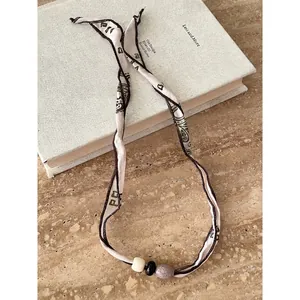 Dettaglio collana etnica in tessuto con perline sopra un libro di design.