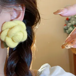 Detail view of a yellow flocked flower stud earring on a model's ear in warm light.