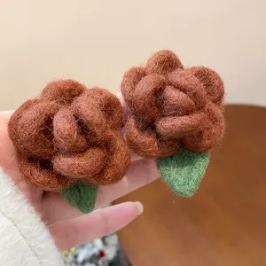 Close-up of brown flocked flower stud earrings with green leaf detail and soft texture.