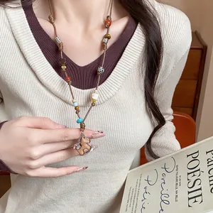 Close-up of a hand-woven rocking horse pendant necklace styled with a cream sweater