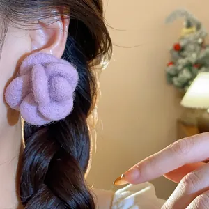 Detailed view of purple flocked flower stud earrings with silver needles on an ear