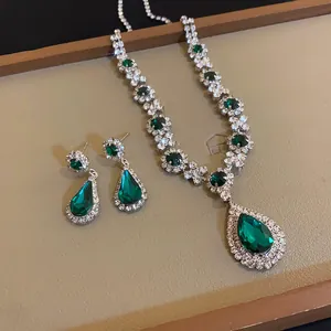 Primo piano di set collana e orecchini in cristallo verde smeraldo su vassoio d'oro