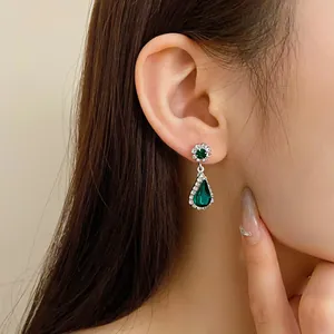Dettaglio di orecchini a goccia color argento con cristalli verde smeraldo su modella