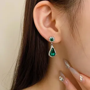 Eleganti orecchini a goccia verde smeraldo con alone di strass indossati sull'orecchio
