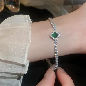 Close-up of silver-toned zircon bracelet featuring a green four-leaf clover pendant.