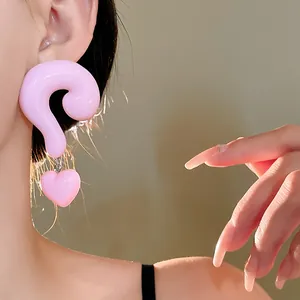 Close-up of pink resin question mark and heart drop earrings on a female model