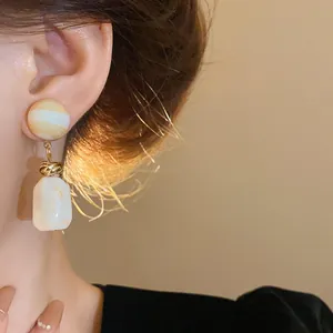Close-up of Maillard-style irregular resin drop earrings worn on a model's ear.