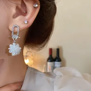 Nahaufnahme eines silbernen Strassohrrings mit einem weißen Blumenanhänger-Detail.