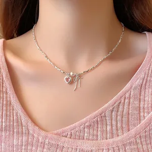 Close-up van zilveren kralenketting met roze hart, parel en strikbedels op een model.