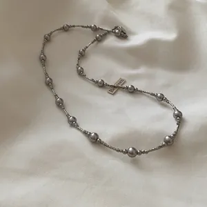Detailopname van elegante zilveren kralenketting met grijze parels op stoffen achtergrond.