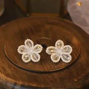 Macro view of crystal flower stud earrings with delicate white bead borders on wood