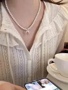 Close-up van een model dat een parelketting draagt met een zilveren strikvormige hanger.