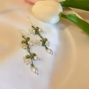 Detailed close-up of vintage French style floral earrings with pearls and green leaves.