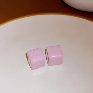 Minimalist pink cube stud earrings with a glossy ceramic finish displayed on white plate