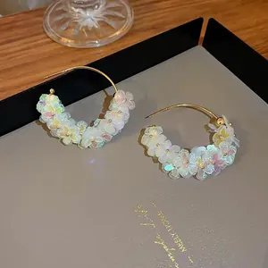 Close-up of floral C-shaped hoop earrings with iridescent resin petals and gold finish.