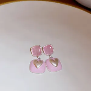 Detail of pink square drop earrings featuring a gold heart and translucent gemstones.